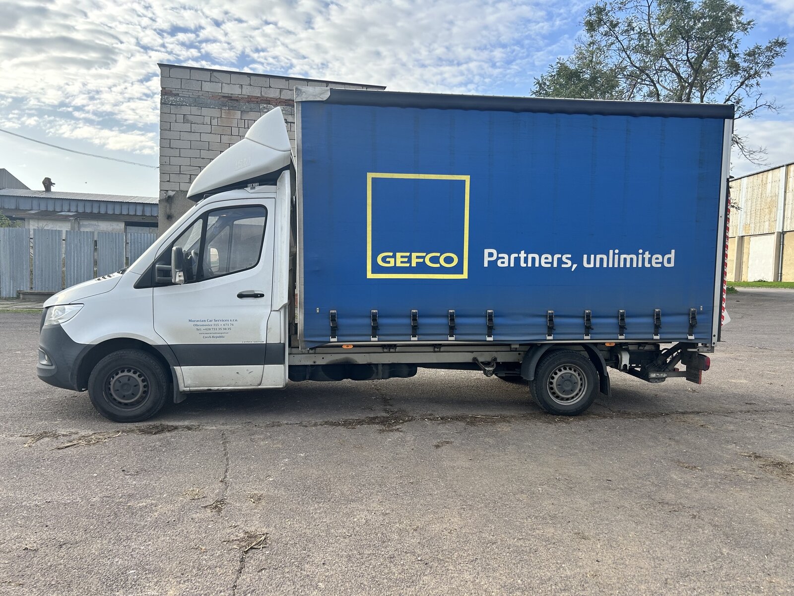 Bílá dodávka Mercedes-Benz Sprinter s modrou plachtovou nástavbou