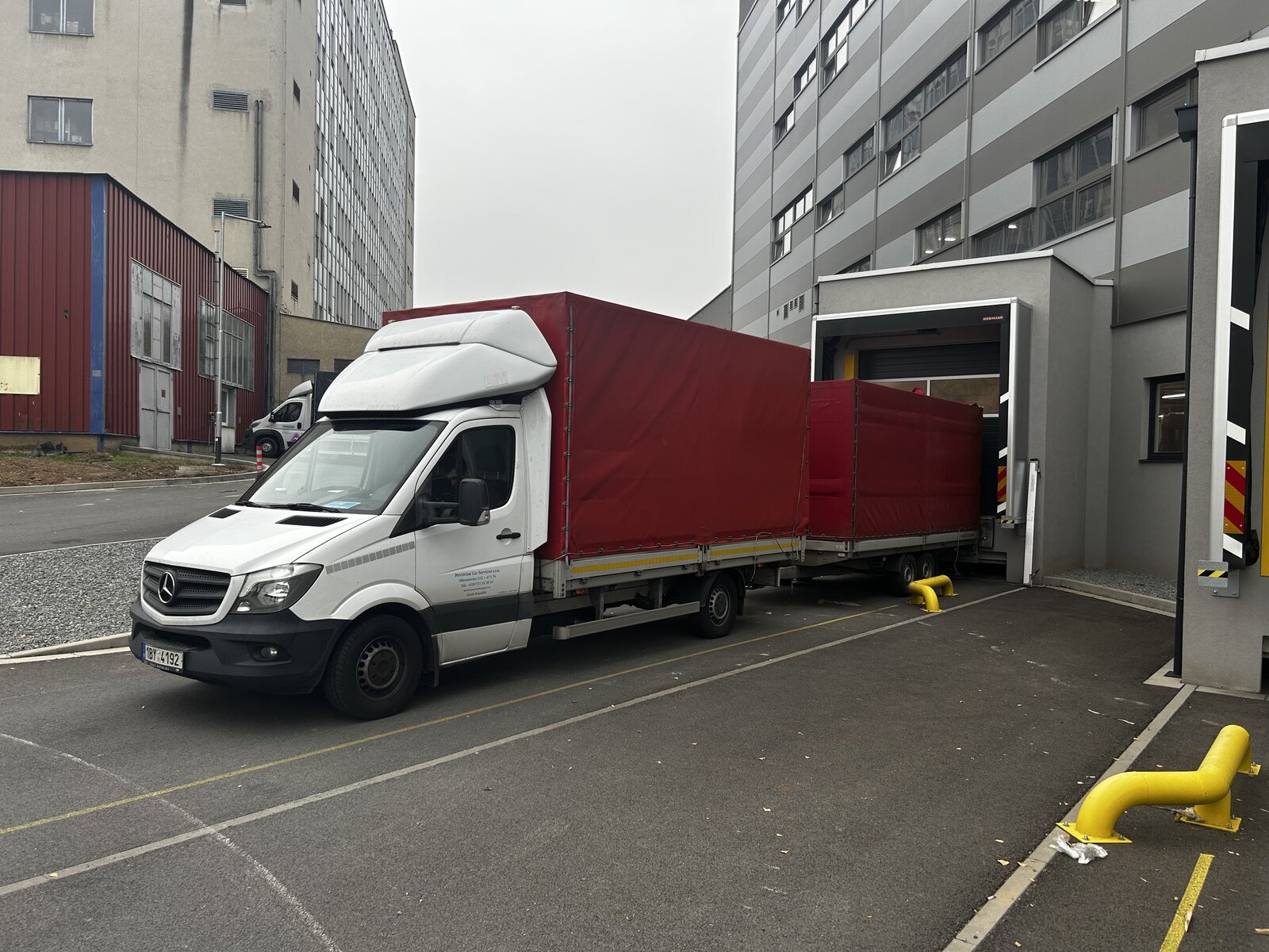 Dodávka Mercedes-Benz Sprinter s červeným plachtovým přívěsem u nakládací rampy