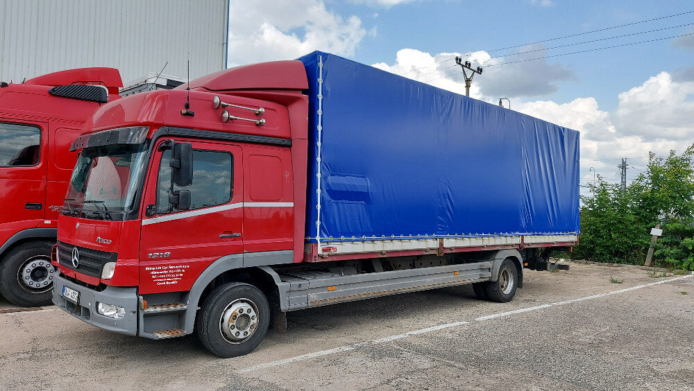 Červený nákladní vůz Mercedes-Benz Atego s modrou plachtovou nástavbou
