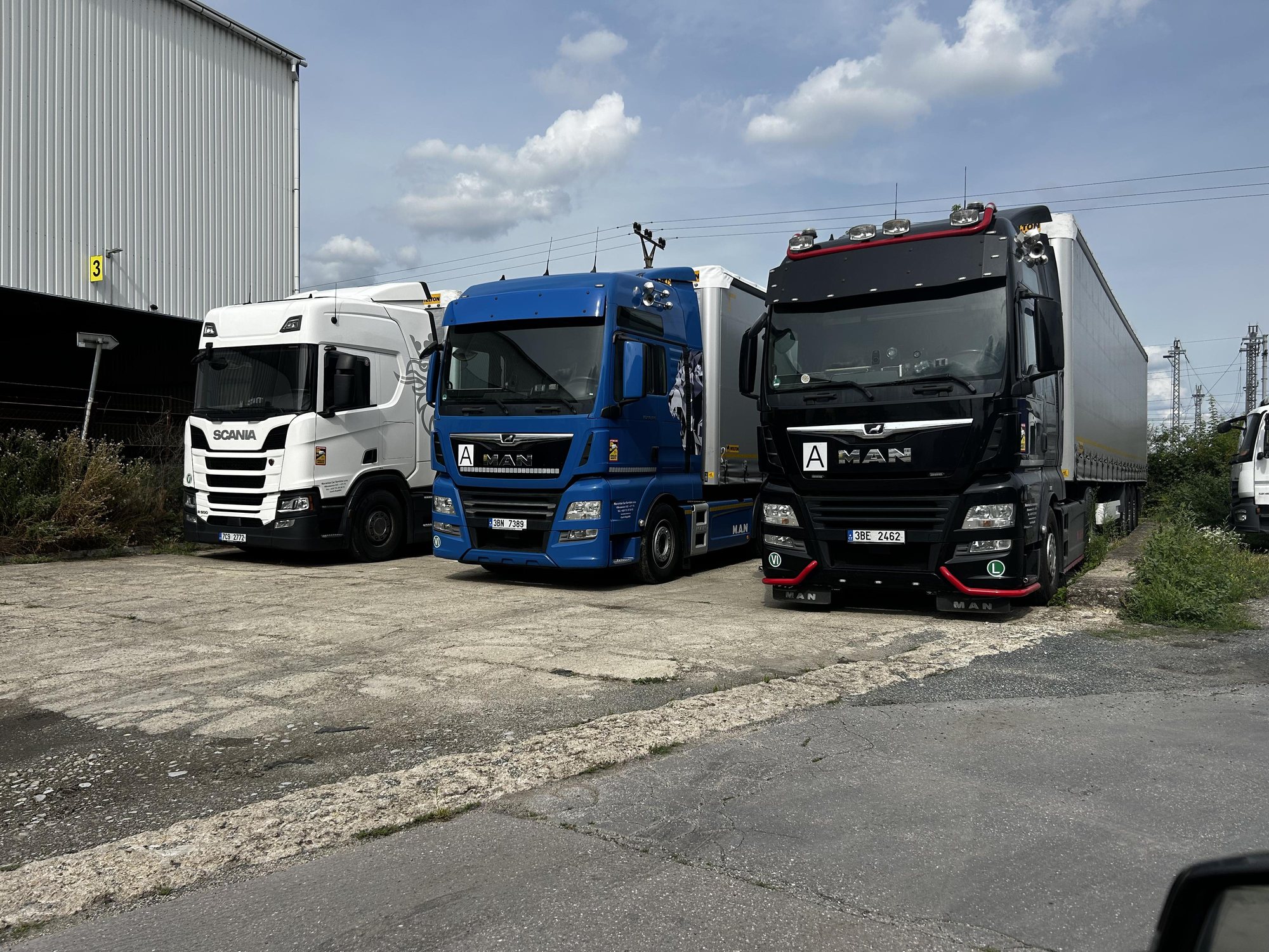 Tři nákladní vozidla společnosti Moravian car services zaparkovaná vedle haly